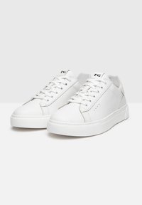 Zapatillas de cuero blanco con un acabado suave, punta redonda, suela plana de goma blanca y diseño de cordones con ojetes. Destacan los acentos de costura.
