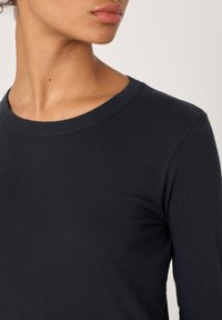 Pika varrukaga tumesinine pluus pehmest puuvillast, millel on ümar kaelus ja õrn tekstuur. Disain võimaldab keha järgivat siluetti.