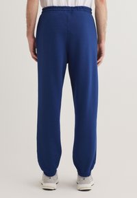 Marineblaue Jogginghosen aus weichem Stoff, mit einem elastischen Bund und schmal zulaufenden Säumen, kombiniert mit hellgrauen Sportschuhen.
