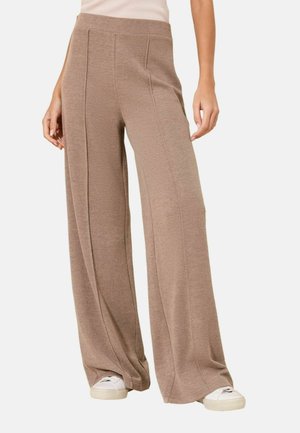 Woman wearing high-waist, wide-leg beige knit pants paired with white sneakers, standing against a plain background.