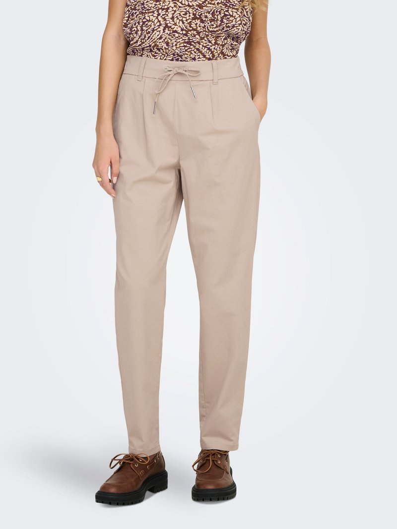 Pantalon beige taille haute avec cordon de serrage et poches latérales, porté avec des chaussures marron à lacets et un haut sans manches à motif.