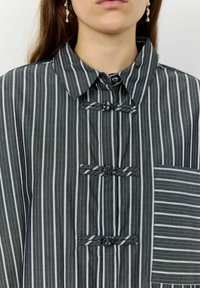 Striped fabric top in dark gray and white, featuring a collar, button closure, and decorative ties. Notable pocket with varied stripe pattern.
