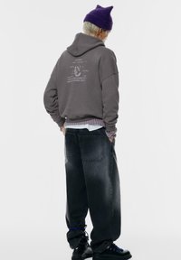 Szary hoodie z nadrukiem z przodu, nałożony na białą koszulę i pasy. Ciemnoniebieskie luźne spodnie dżinsowe, czarne buty z niebieskimi sznurowadłami.