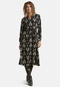 Schwarzes langärmliges Kleid mit einem floralen Muster in Creme- und Blush-Tönen, ausgestattet mit einem Bindegürtel in der Taille und einem ausgestellten Rock.