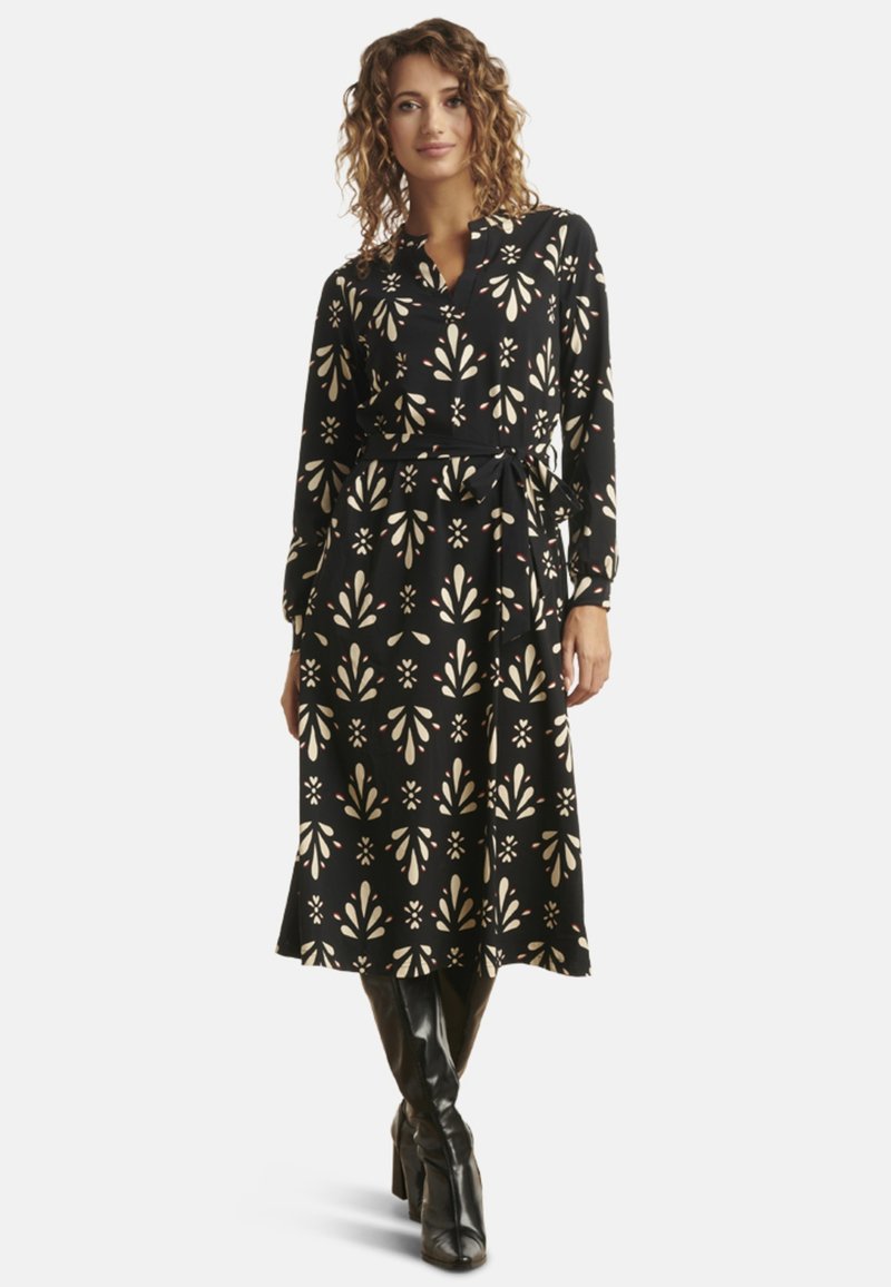 Schwarzes langärmliges Kleid mit einem floralen Muster in Creme- und Blush-Tönen, ausgestattet mit einem Bindegürtel in der Taille und einem ausgestellten Rock.