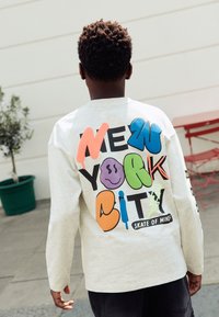 Lysegrå langærmet sweatshirt med farverig, stiliseret tekst "NEW YORK CITY" og legende grafik. Velegnet til afslappet brug.