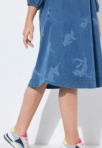 Denim-mekko keskisinisessä, jossa on kala-kuvioita, lyhyet hihat ja levenevä malli. Yhdistetty monivärisiin lenkkareihin, joissa on valkoinen pohja.