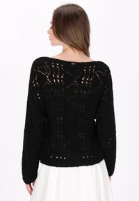 Schwarzer gestrickter Pullover mit lockerer Passform, weitem Ausschnitt und kunstvollem Lochmuster. Lange Ärmel enden an den Handgelenken.