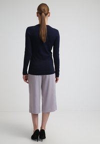 Top a maniche lunghe blu navy, tessuto leggero, pantaloni culotte grigi a gamba larga, tacchi neri. Vista posteriore con trama minima e senza motivi visibili.