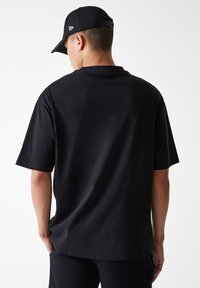 Black short-sleeve t-shirt in a relaxed fit, featuring a smooth texture. Worn with a black cap displaying a logo on the back.