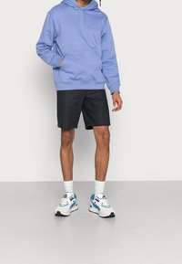 Vaaleansininen huppari, jossa on etutasku, yhdistetty mustiin shortseihin ja monivärisiin lenkkareihin. Mukana valkoiset nilkkasukat ja rento malli.