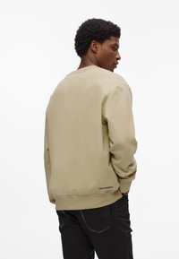Sudadera color beige claro con cuello redondo, mangas largas y puños acanalados. Presenta un logo sutil en el dobladillo, hecha de una tela suave.