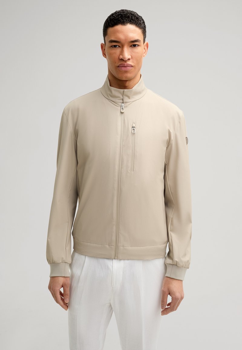 Beige lichtgewicht jack met een hoge kraag, een ritssluiting aan de voorkant en elastische manchetten. Beschikt over een ritsborstzak en een zachte textuur.