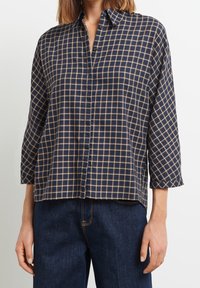 Chemise à carreaux bleu marine et beige, à boutons, manches longues, tissu doux, coupe décontractée, avec un col classique et des boutons à l'avant.