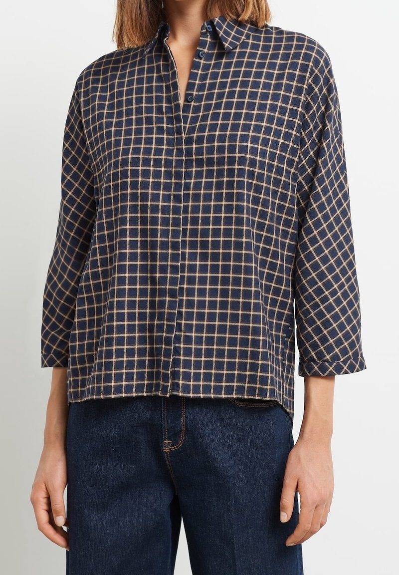 Chemise à carreaux bleu marine et beige, à boutons, manches longues, tissu doux, coupe décontractée, avec un col classique et des boutons à l'avant.