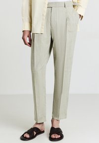 Pantaloni beige a vita alta con sottili righe, abbinati a sandali intrecciati marrone scuro e una camicia crema con bottoni.
