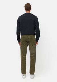 Dunkelblauer Crewneck-Pullover kombiniert mit olivgrünen Cordhosen. Weiße Sneaker mit goldenen Akzenten runden das Outfit ab, Ansicht von hinten.