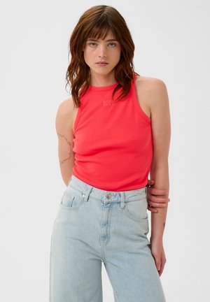 Korallenrotes ärmelloses Tanktop mit gerippter Struktur und hohem Ausschnitt, kombiniert mit hellblauen, hoch taillierten Jeans.