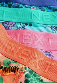 Három színes alsónemű derékpánt, lila, zöld és rózsaszín színben, dombornyomott "NEXT" felirattal, egy állatos mintázatú textílián. 