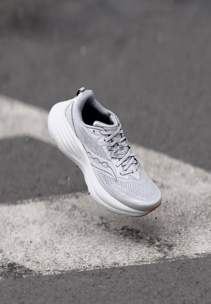 Chaussure de course légère en mesh gris avec une semelle blanche rembourrée, présentant des détails subtils et des accents texturés dans l'ensemble.