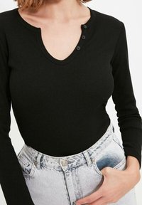 Svart ribbad långärmad topp med V-ringning och tre knappp Det som bärs med högmidjade ljusblå denimshorts.