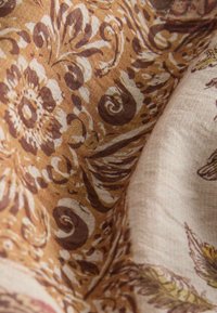 Tissu marron et beige avec des motifs floraux et cachemire complexes, présentant des motifs tourbillonnants et feuillus détaillés.
