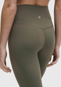 High-waisted, olive-green leggings made of smooth, stretchy fabric, featuring a subtle logo and double-stitched seams for durability.