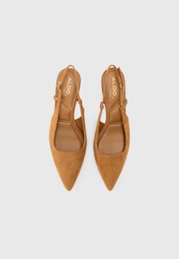Vaaleanruskeat mokka-slingback-kengät, joissa on teräväkärkiset varpaat, säädettävät nilkkahihnat ja sileä sisustus. Logo on kohokuvioitu sisäpohjassa.