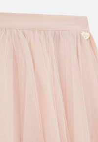 Gonna in tulle rosa chiaro, caratterizzata da un tessuto trasparente a strati, una vita liscia e un piccolo logo dorato a forma di cuore.