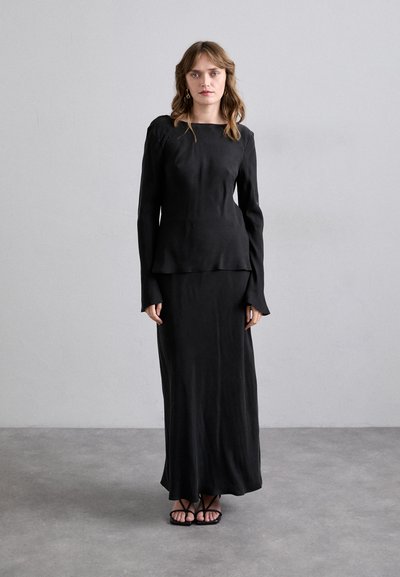 Haut noir à manches longues avec un décolleté bateau et un ourlet fluide, associé à une jupe maxi ajustée assortie et des sandales minimalistes à lanières.