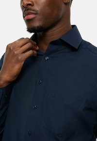 Marineblauw button-up shirt met een puntige kraag, borstzak en bijpassende knopen; gladde, effen stof zonder patronen of texturen.