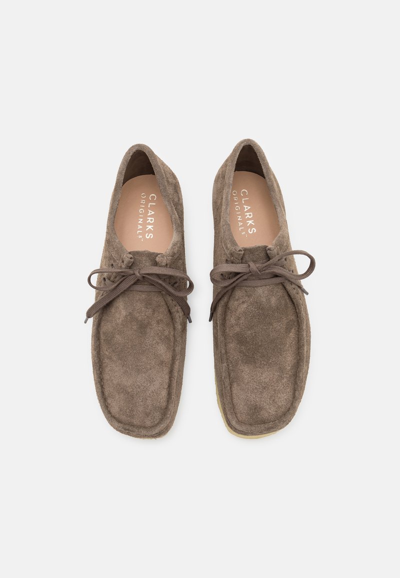 Braune Wildlederschuhe mit runden Zehen, dünnen Schnürsenkeln und weichem Material. Verfügt über eine hellfarbige Sohle und ein geprägtes Markenlogo im Inneren.