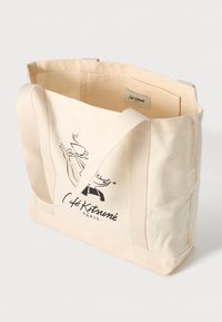 Kanvas totebag i lys beige med lange håndtak. Har en svart illustrasjon og teksten "Café Kitsuné Paris" på den ene siden.