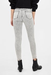 Šedé pruhované úzké džíny s bílými svislými pruhy, vysokým pasem a dvěma zadními kapsami, spárované s černými kotníkovými botami.