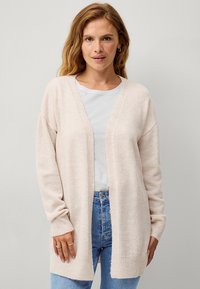 Cardigan rosa chiaro, con apertura frontale, polsini e orlo a coste, texture morbida, indossato sopra una t-shirt grigia chiaro, abbinato a jeans blu.