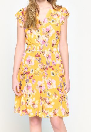 Yellow floral dress with pink, white, and purple flowers, flutter sleeves, V-neck, and elastic waist worn by a standing person.