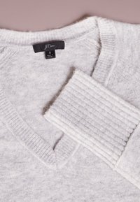 Suéter gris claro de cuello en V hecho de material suave, con puños acanalados y etiqueta que dice "J. Crew" talla pequeña. Patrón texturizado visible.