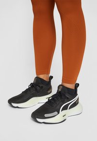 Schwarze Sportschuhe mit grauen und weißen Akzenten, strukturiertem Obermaterial und dicker, weißer Sohle. Getragen mit orangen engen Leggings.