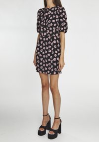 Vestido negro con patrones florales en rosa, mangas cortas abullonadas, un corsé ajustado y una falda acampanada, combinado con tacones de plataforma negros.