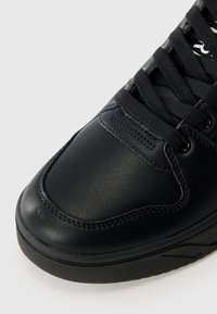 Μαύρο δερμάτινο αθλητικό παπούτσι με στρογγυλή μύτη, υφή ανώτερης επιφάνειας, επίπεδες μα�ύρες κορδόνες και λείος καουτσούκ σόλα με διακριτές αυλακώσεις για πρόσφυση.