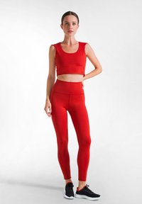 Rode cropped tanktop gecombineerd met hoge rode leggings; beide gemaakt van rekbaar materiaal. Zwarte sportschoenen met rode accenten.