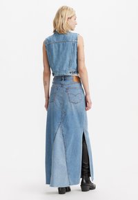 Denim vest en lange rok set in lichtblauw, met een ruwe zoom en zijsplit. Heeft contrasterende panelen en een leren merkembleem op de achterkant.