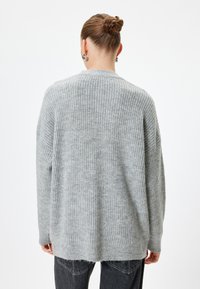 Grå stickad tröja med lös passform, ribbat mönster och sänkta axlar. Har en rak fåll och långa ärmar.