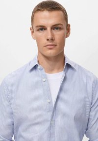 Gestreifte Hemdbluse aus blau-weißer Baumwolle mit Kragen und lockerer Passform, über einem weißen T-Shirt getragen.