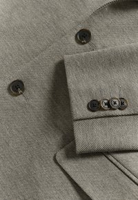 Materialul în dungi gri are un rever croit și cinci butoane negre pe manșetă, evidențiind un design curat și structurat.