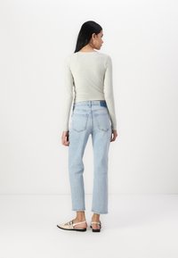Haut à manches longues gris clair, jeans taille haute bleu clair avec des poches arrière distinctives, et ballerines adaptées couleur nude avec des bouts et des lanières noires.