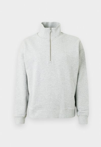 Svetlosivý mikina s vysokým golierom a polovičným zipsom, dlhými rukávmi a diskrétnym vyšitým logom na hrudi. Mäkčený povrch.