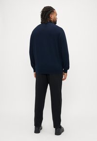 Maglione lavorato a maglia blu navy con collo tondo e maniche lunghe, indossato con pantaloni neri e scarpe nere, caratterizzato da una vestibilità comoda e una texture liscia.
