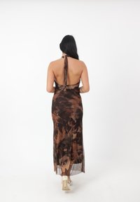 Brun og tan blomstret maxi-kjole med halterneck-design og åben ryg, der har en flydende stoftekstur.
