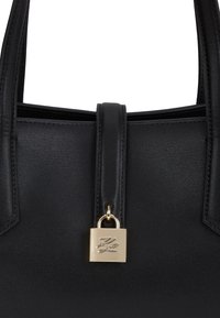 Svart lærveske med en gull firkantet lås gravert med en stilisert dobbel "K" på frontstroppen.